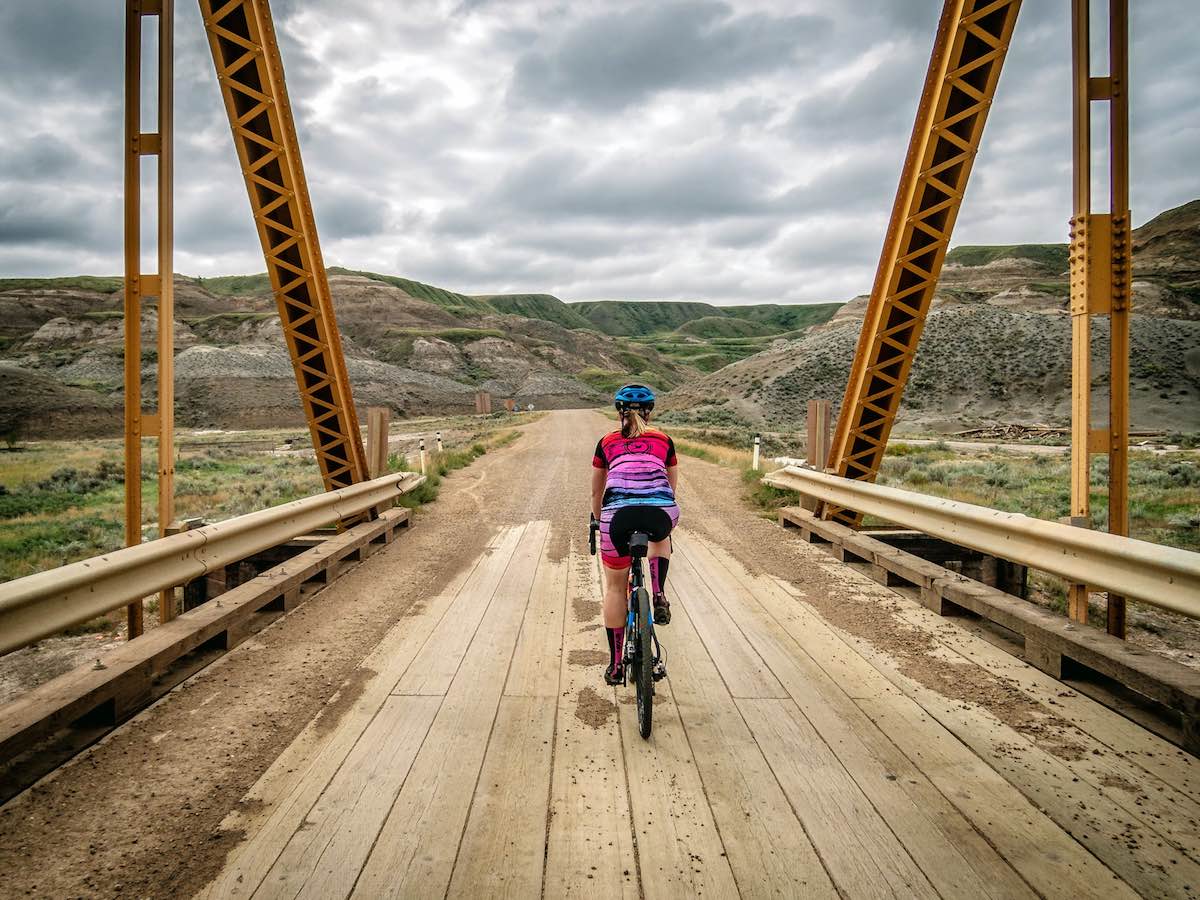 bikerumor pic of the day cyclist riding over wooden bridge into the badlands of Drumheller, Alberta, Canada.