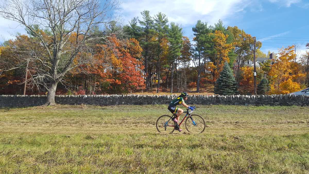 bikerumor pic of the day fruitlands CX race in Harvard, Massachusetts, cyclist on grass field with fall trees in the background.