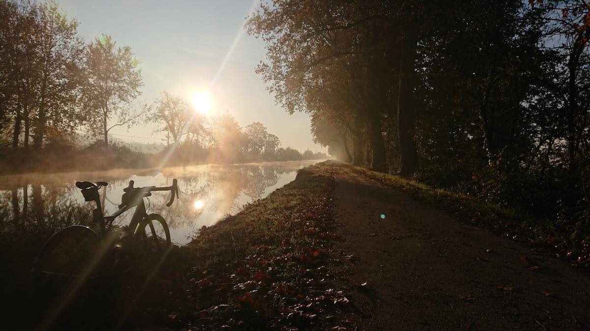 bikerumor pic of the day silhouette of a bicycle in lower left corner as sun rises over the foggy canal behind it.
