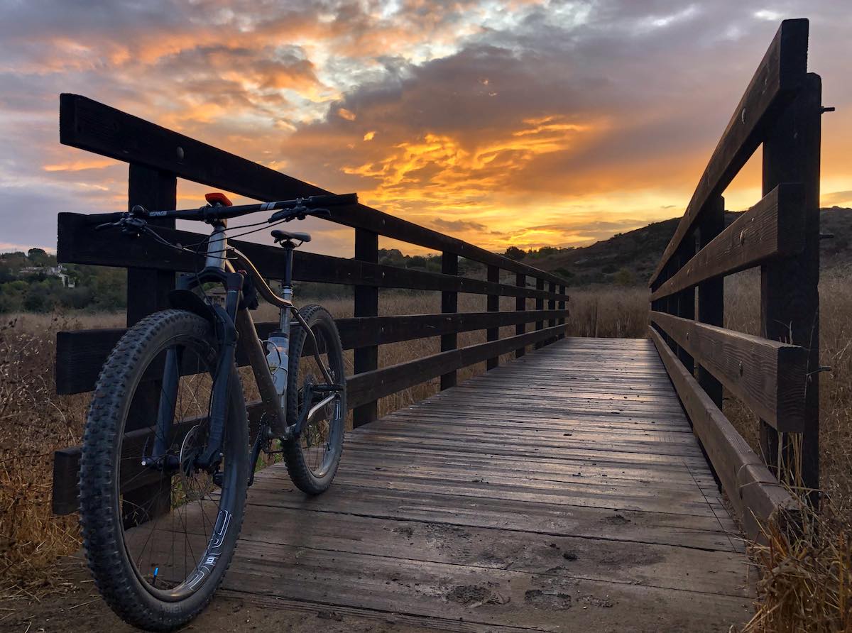 bikerumor pic of the day Bommer Meadows, Irvine california, mountain bike is leaning against a wooden bridge with fiery orange sunrise in the background.