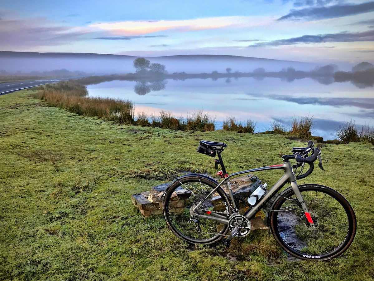 bikerumor pic of the day bicycle in Cefn Bryn, Gower, South Wales UK. Bicycle is sitting on green grass with lake in the background reflecting the gray sky.