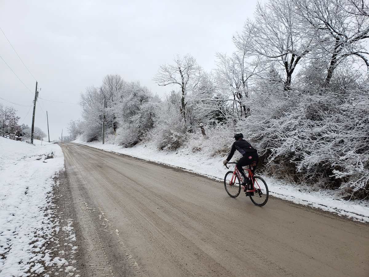 bikerumor pic of the day cyclist riding up a packed dirt road with snow covering the trees and edges of the road.