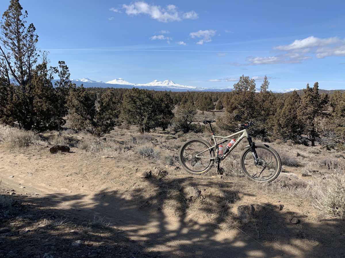 bikerumor pic of the day mountain biking in Maston trail system in Central Oregon. mountain bike on dirt trail with pine scrub behind it and snowy mountain tops in the distance.