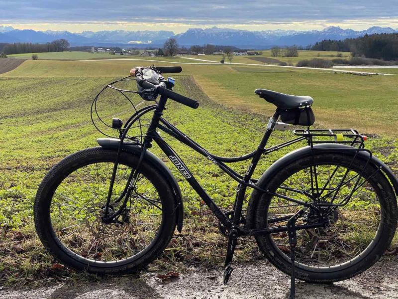 black jones touring bicycle on gravel trail in front of fields with snow capped mountains on the horizon. Southern German foothills.