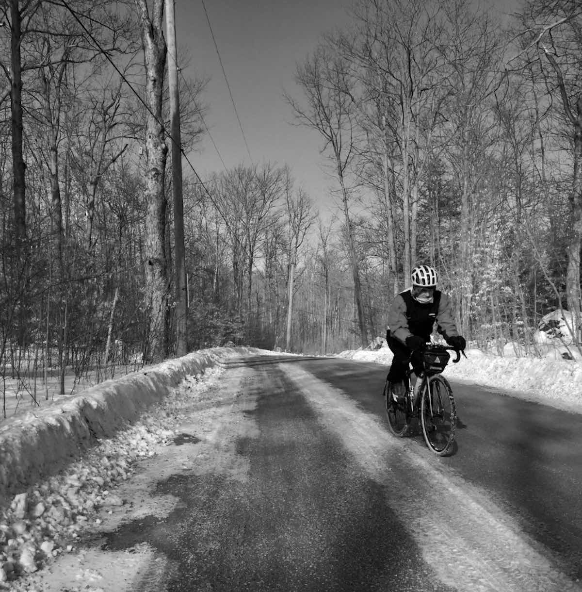 bikerumor pic of the day cyclist riding in -15 degree celsius weather on a road covered in snow, bare trees on either side of the road.
