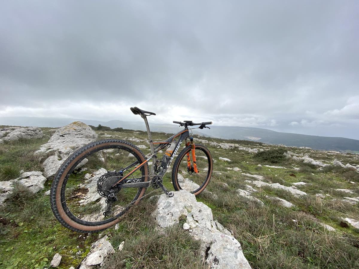bikerumor pic of the day Serras de Aire and Candeeiros Porto de Mós Nature Park Portugal. Mountain bike looking out over rocky vegetation with mountains in the distance, clouds hanging low in the sky.