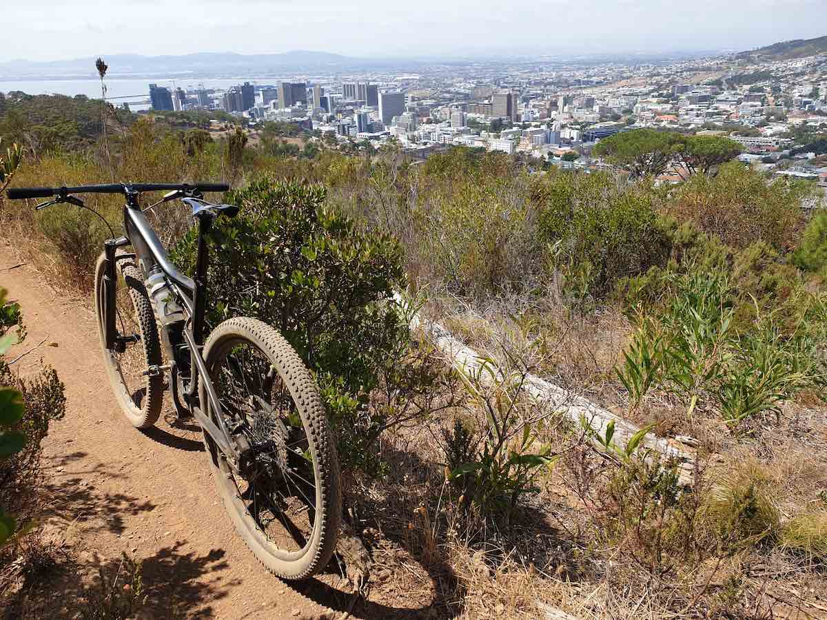 bikerumor pic of the day mountain bike on a dirt trail to the left of the photo, trail drops off to the right into scrub land overlooking the city of cape town south africa.