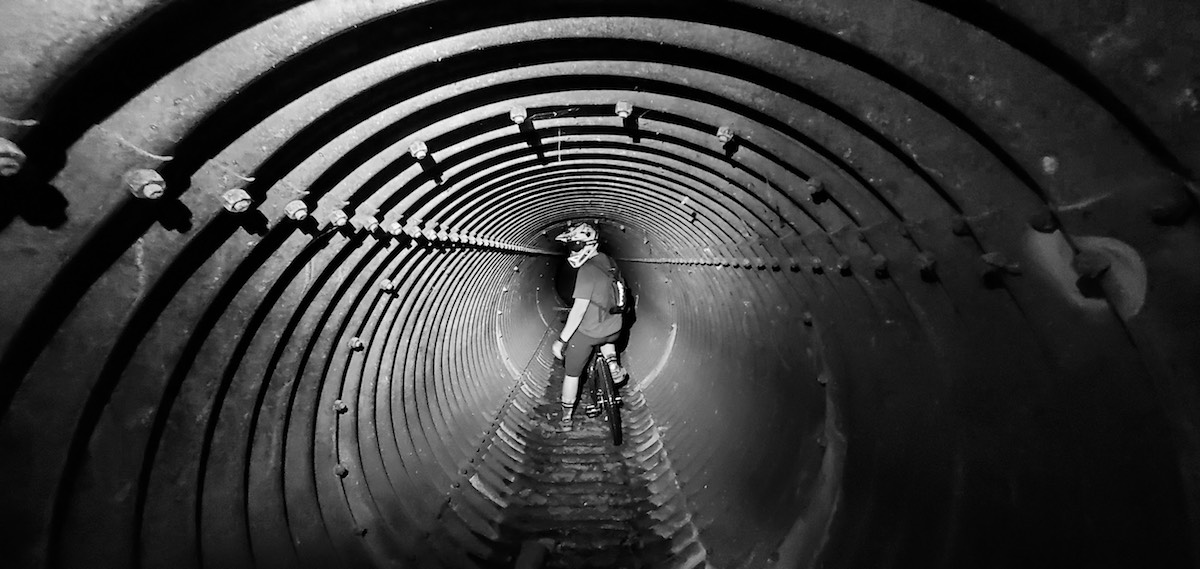 bikerumor black and white pic of the day mountain biker halfway through a corrugated metal tunnel stopped and looking back at photographer in Kailua, Oahu, Hawaii.
