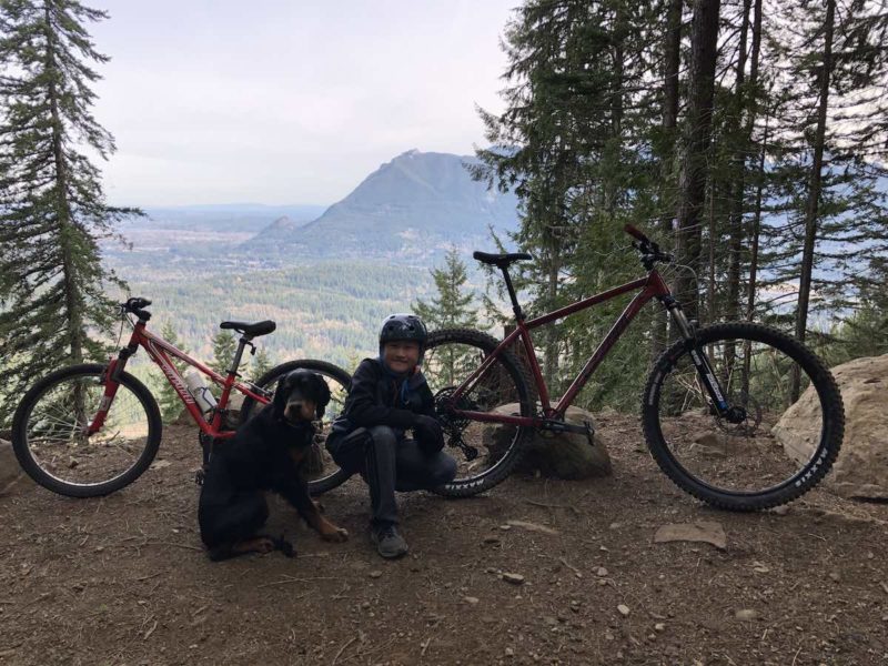 bikerumor pic of the day Olallie Trail - North Bend, Washington, two bicycles posed with a boy and his dog between them on a break in the pine trees overlooking a valley below.