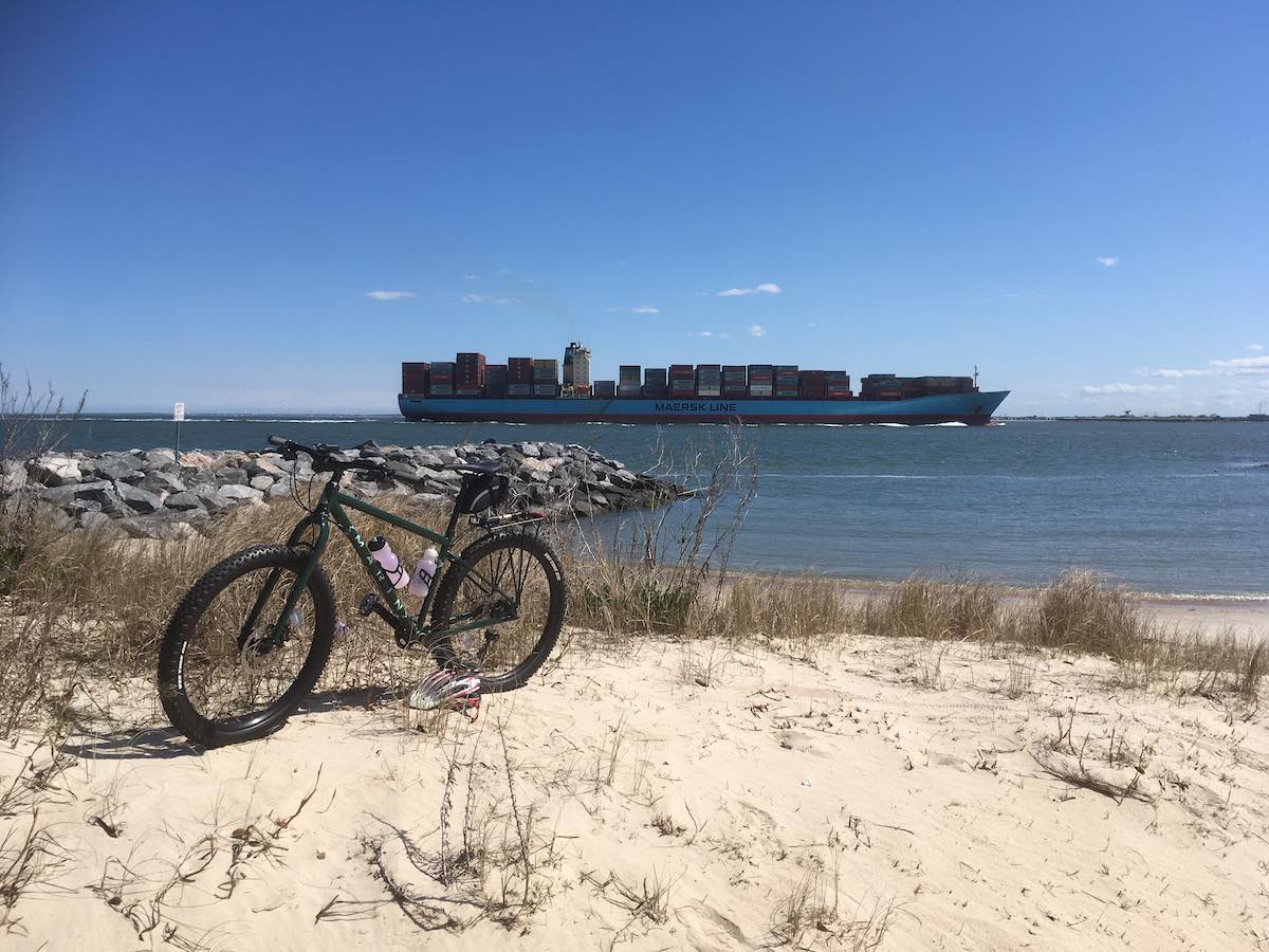bikerumor pic of the day fort monroe virginia, bicycle on the sand with a large tanker ship in the ocean in the background.