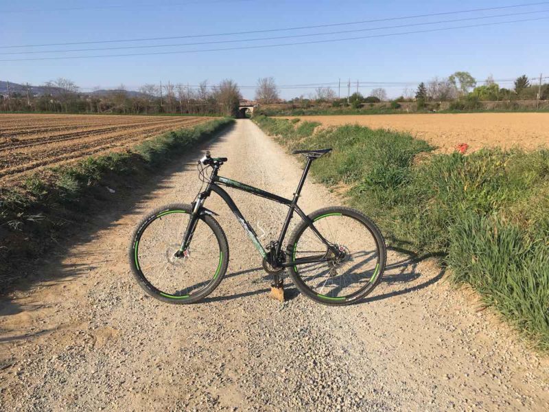 bikerumor pic of the day specialized hard rock bicycle posed in the middle of a hard packed gravel road with fields on either side and a bridge crossing the road in the distance. Northern Italy.