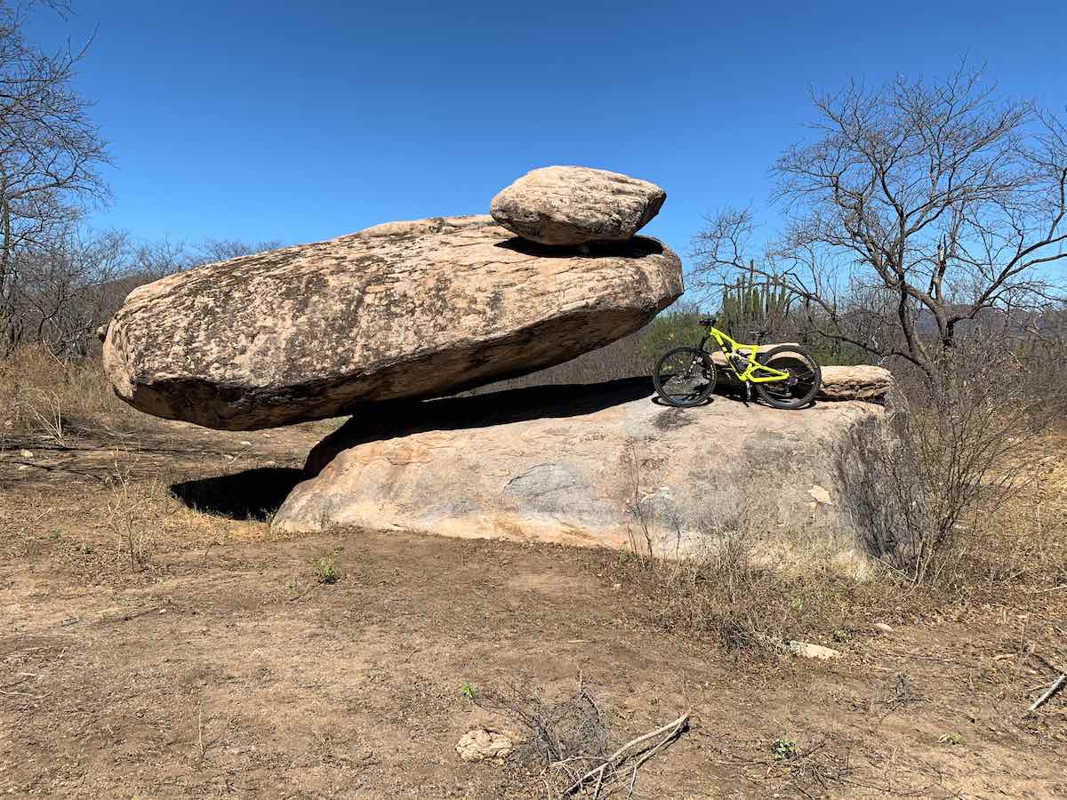 bikerumor pic of the day mountain biking in mexico, navojoa sonora, yellow bike sitting on top of a large boulder with another large boulder balancing on top of the first boulder.