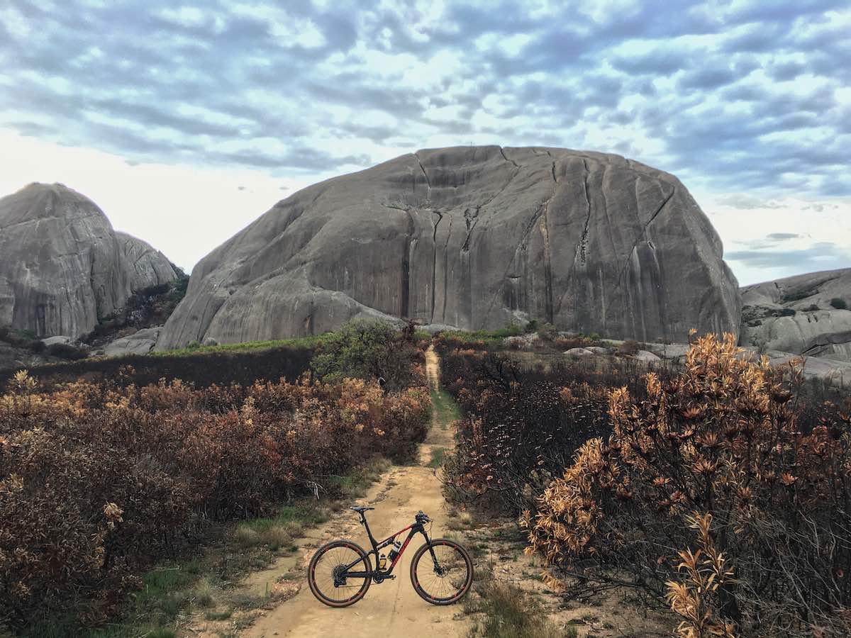 bikerumor pic of the day mountain bike posed on a dirt path leading up to large igneous rock formation like a tortoise shell with burnt brush on either side, paarl mountain in south africa.