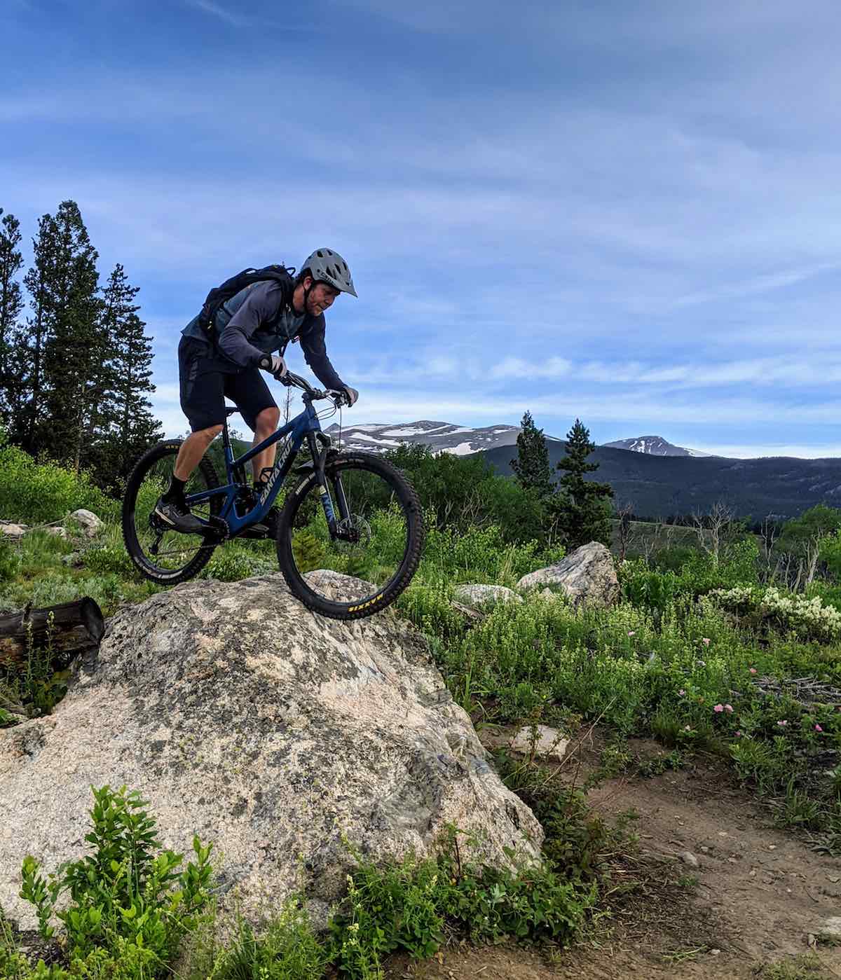 bikerumor pic of the day nederland colorado mountain biker descending a large boulder with a dirt trail and green fields beyond.