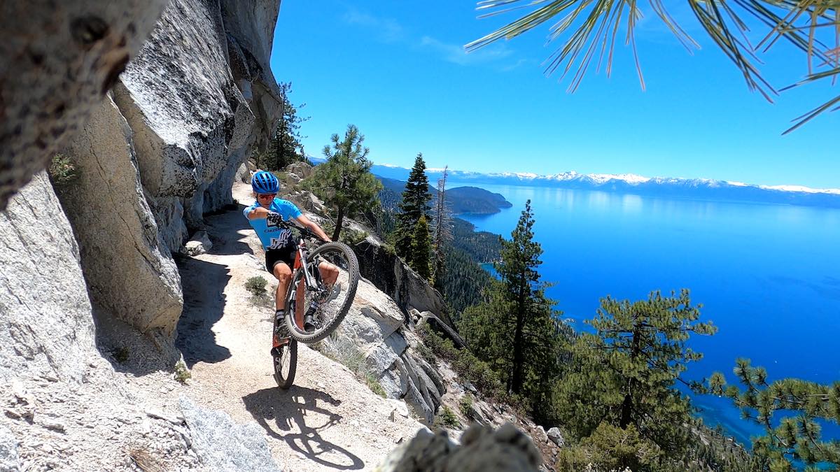 bikerumor pic of the day mountain biker doing a wheelie on the flume trail with lake tahoe in the distance.