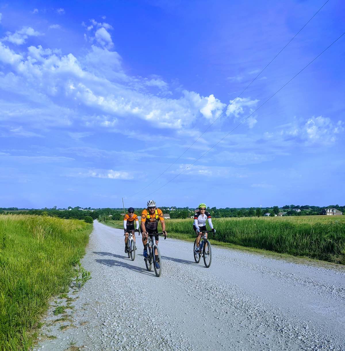 bikerumor pic of the day johnson county kansas three cyclists riding on a gravel road with green fields on either side and wide expanse of blue sky.