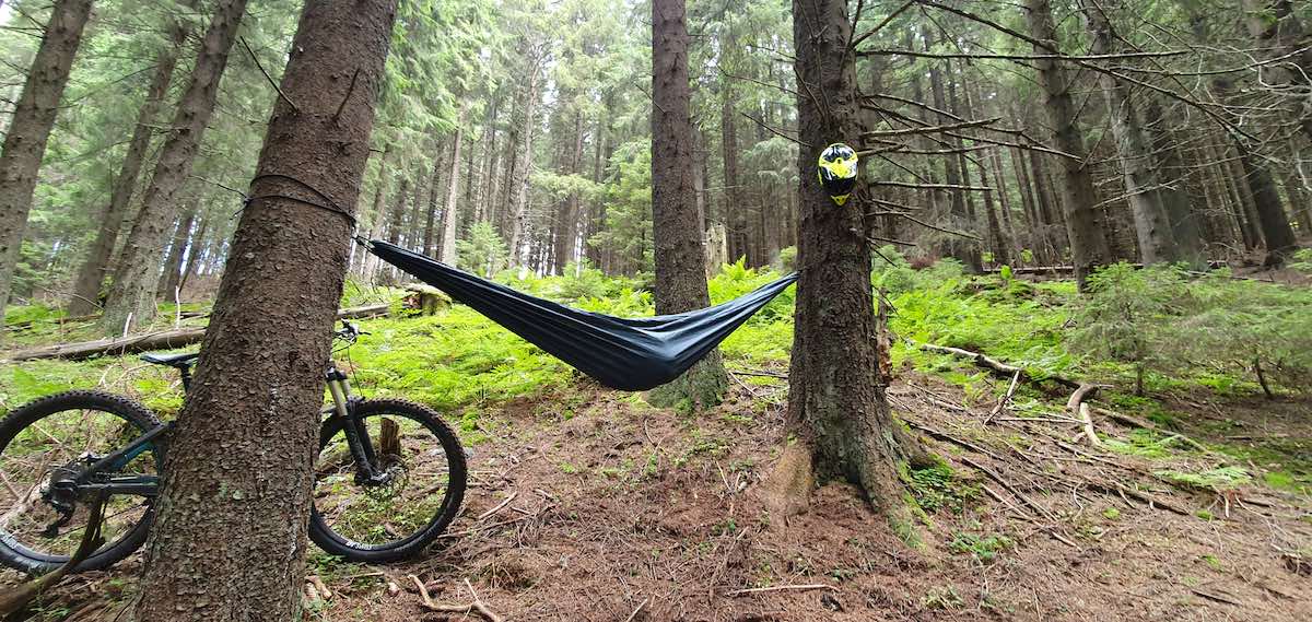 bikerumor pic of the day mountain bike leaning against a large tree trunk with hammock attached to it in the middle of the woods in Parâng Mountains, Romania.
