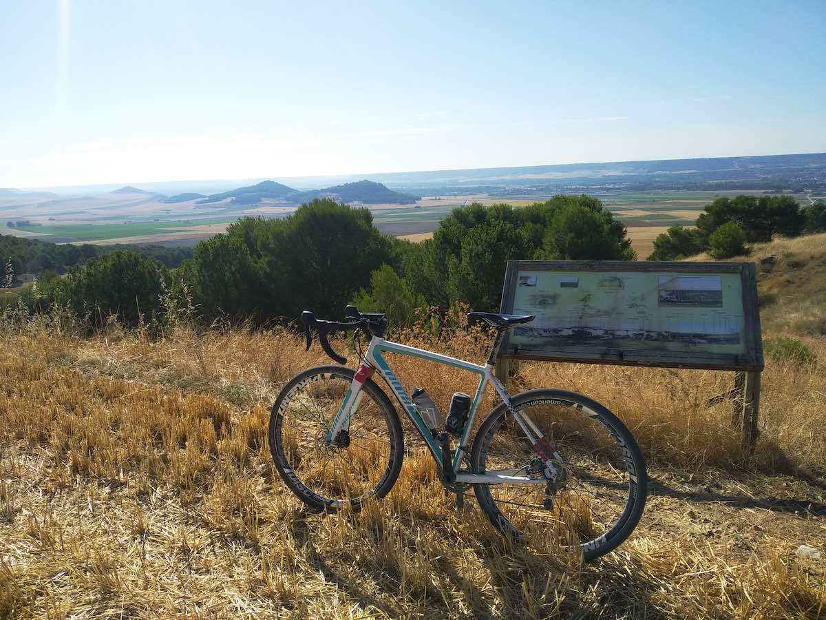 bikerumor pic of the day niner in a dried field looking over long expanse of flat lands dotted with green troves of trees in spain.