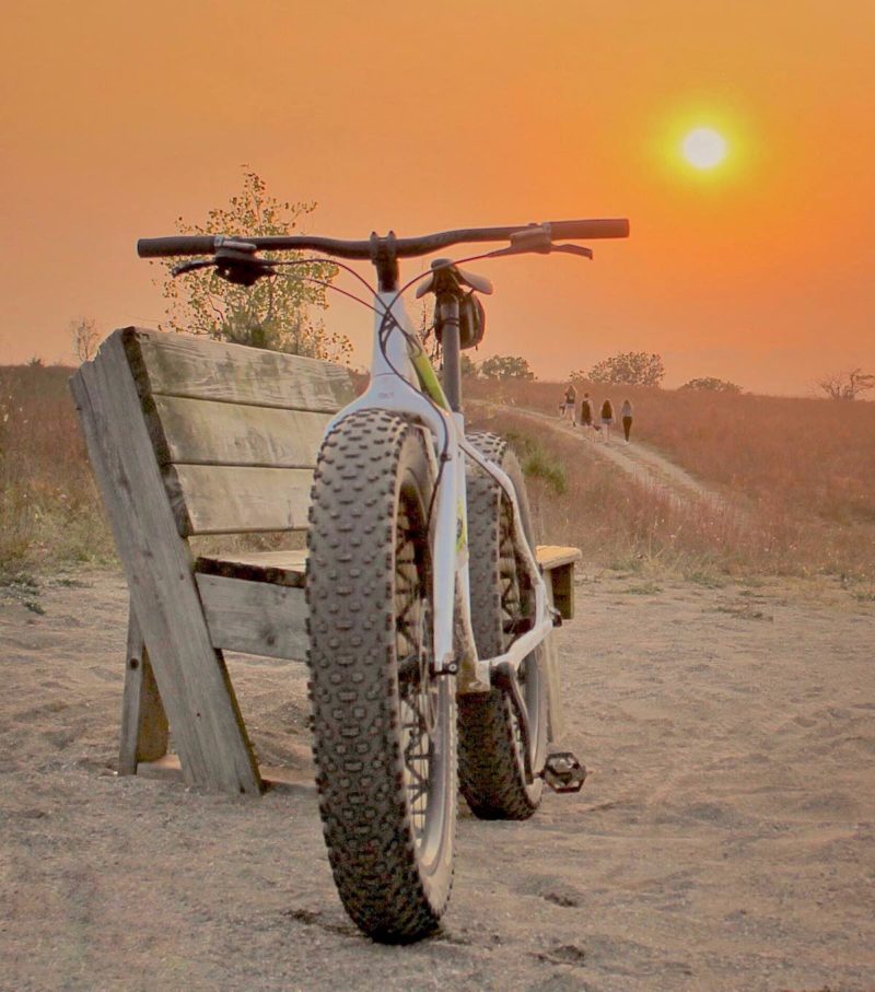 bikerumor pic of the day fat bike leaning against a wooden bench in the sand with a smoky orange haze in the sky at sunset in island lake recreation area in brighton michigan