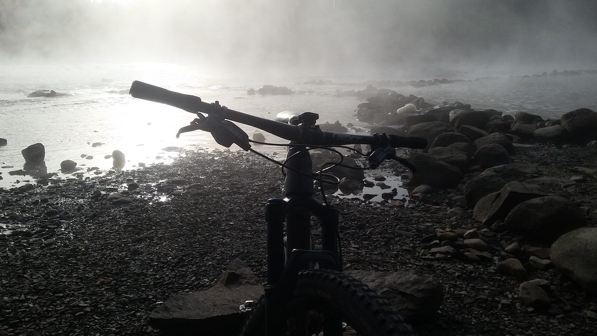bikerumor pic of the day black and white photo of a bicycle in the foreground with the magog river with rocks and smoky haze in the background in sherbrooke quebec canada.