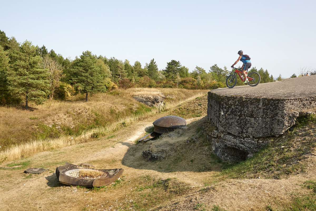 bikerumor pic of the day verdun battlefield in france a biker looks out from the top of an exploded bunker over shards of metal bunker pieces below and a low pine forest.