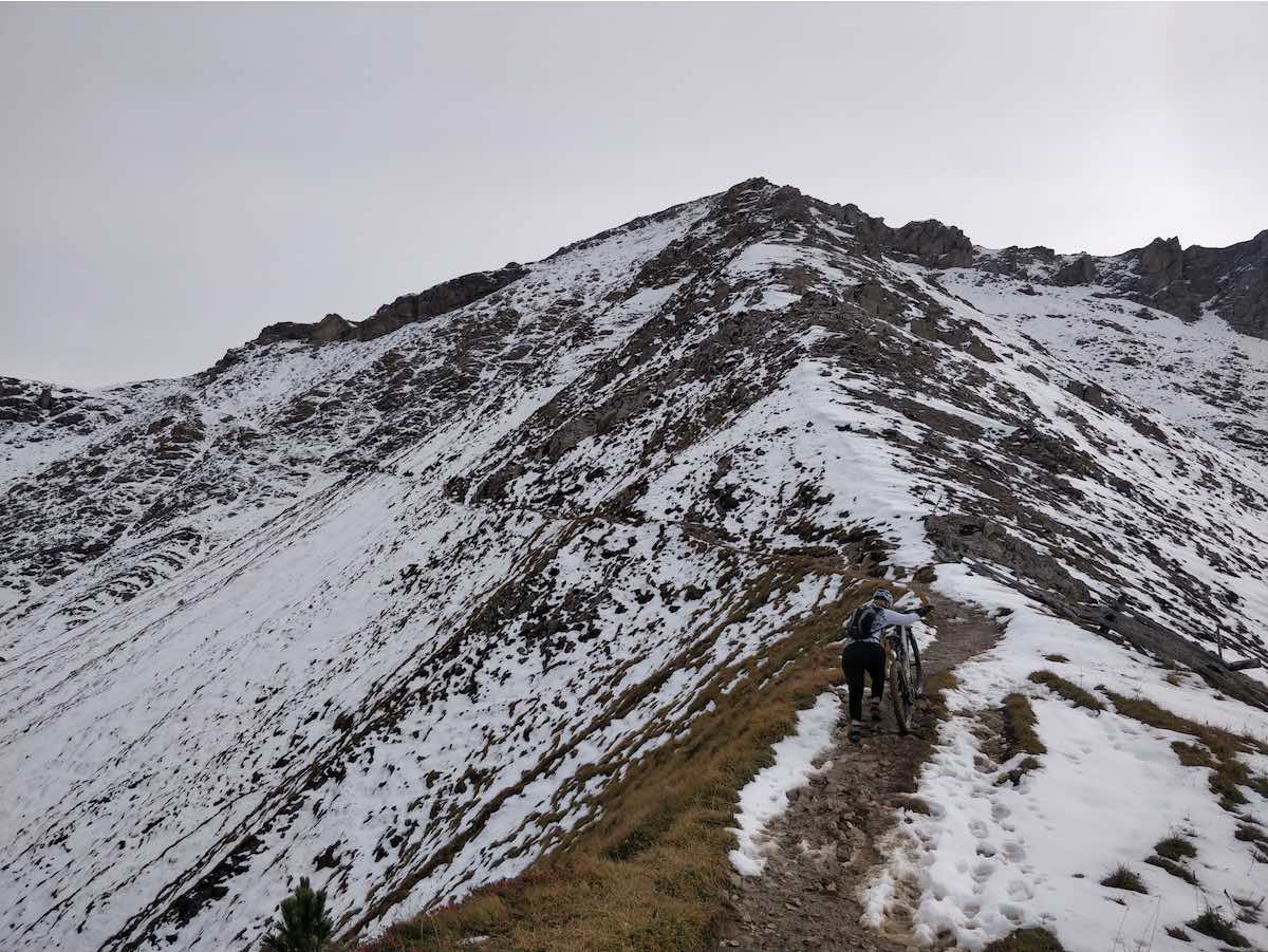 bikerumor pic of the day mountain biking on steep mountain top cyclist has dismounted and is pushing the bike on the snow speckled trail.