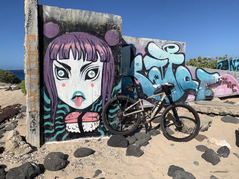 bikerumor pic of the day bicycle leaning against a concrete barrier on a beach that has been painted with graffiti and anime character.