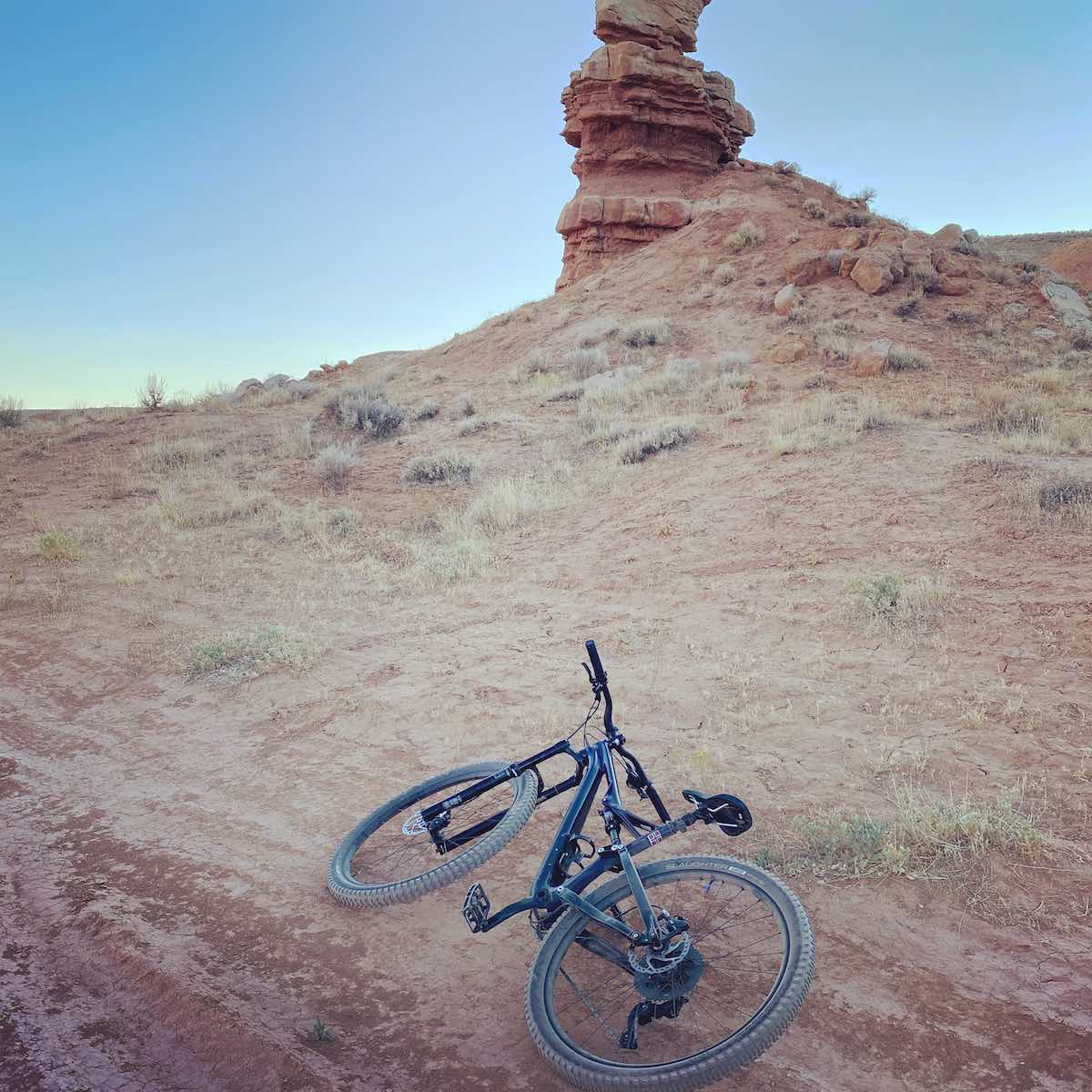 bikerumor pic of the day mountain bike laying on the side of the trail of mccoy flats in vernal utah the land is mostly red dirt with some scrub brush looking up to a hoodoo land feature.