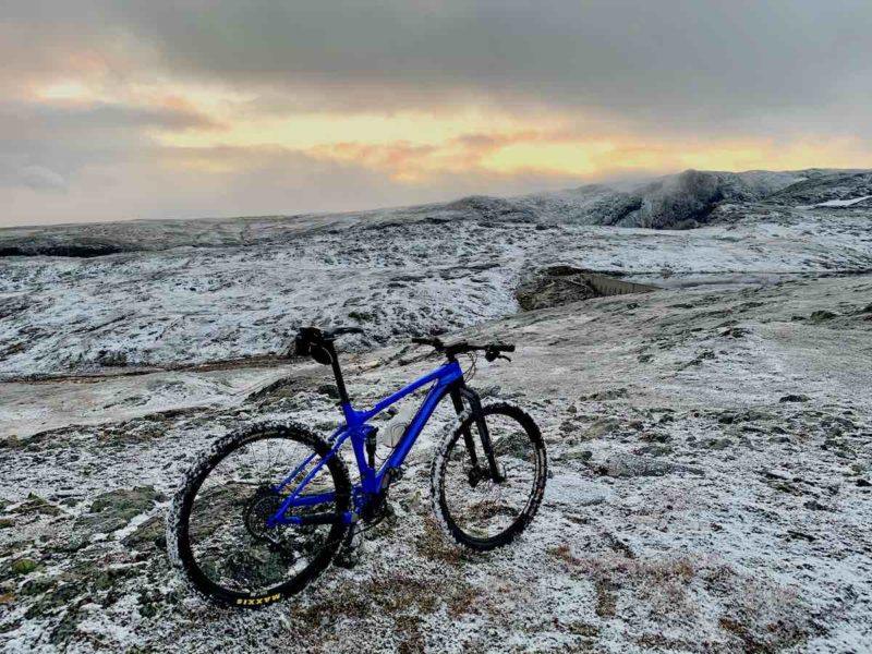bikerumor pic of the day blue bicycle on frozen tundra ground no trees for as far as you can see with a grey sky with orange glow in the distance.
