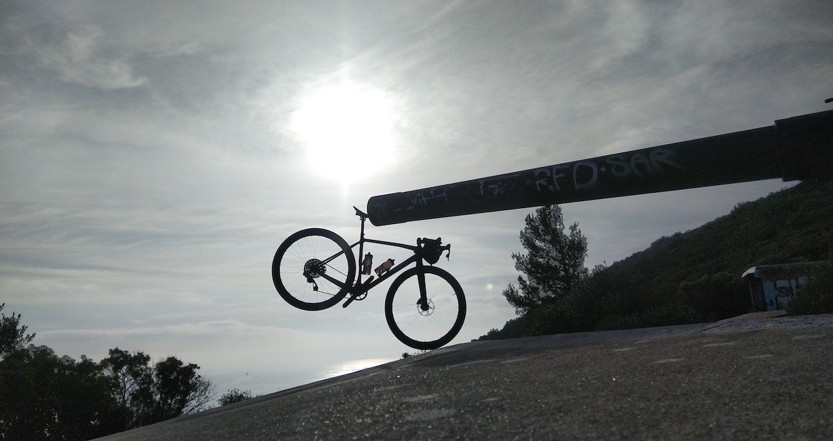 bikerumor pic of the day a bicycle hangs from the end of a long cannon in profile with the bright sun behind it in what looks like a black and white image.