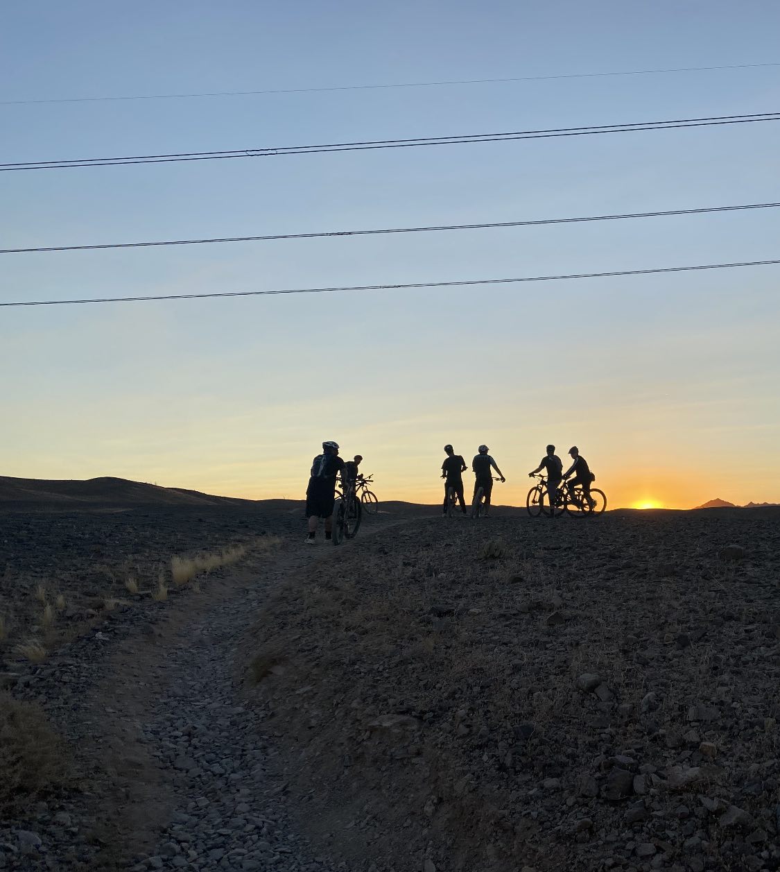 bikerumor pic of the day a group of cyclists gather at the top of a hill there is the sun peeking out from beyond their silhouettes with a blue sky above.