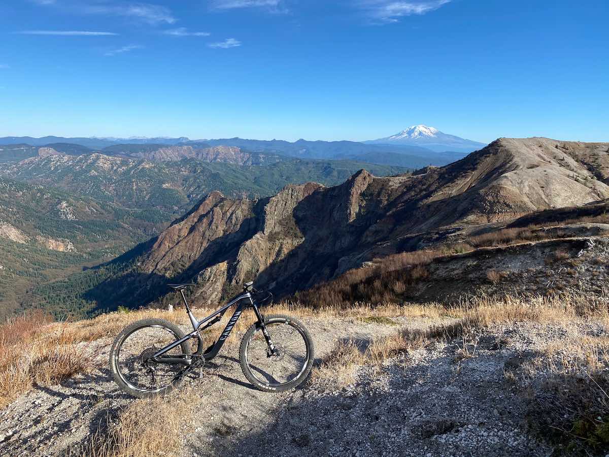 bikerumor pic of the day bicycle on the grassy edge of a mountain overlooking another mountain and mount saint helens in the distance.