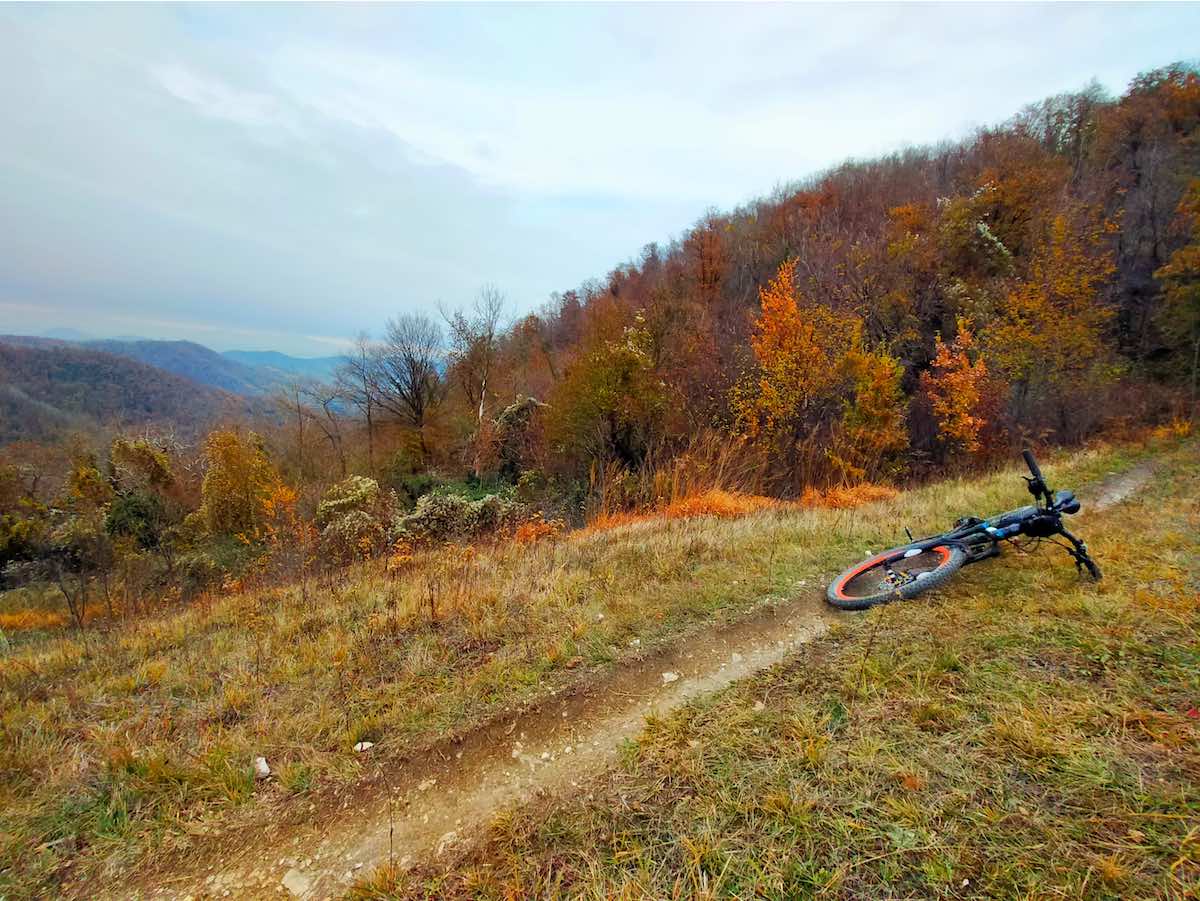bikerumor pic of the day a mountain bike lays aside a dirt path on a field on the slope of a mountain with trees in the distance full of fall colors at Parco Regionale dei Colli Euganei in padua italy.