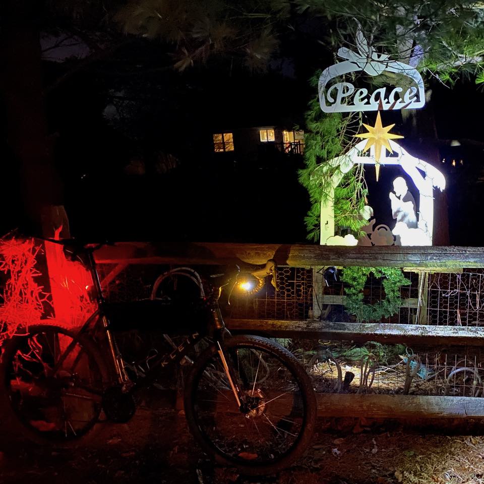 bikerumor pic of the day at night a klein bicycle is resting against a wood fence where a small metal nativity scene is placed with the word Peace above it.