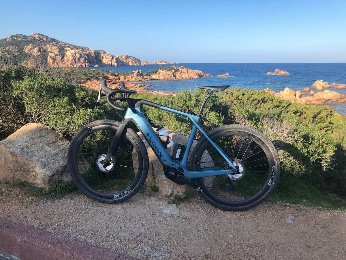 bikerumor pic of the day canyon bike is posed leaning on large boulder with brush behind it and a body of water in the background.