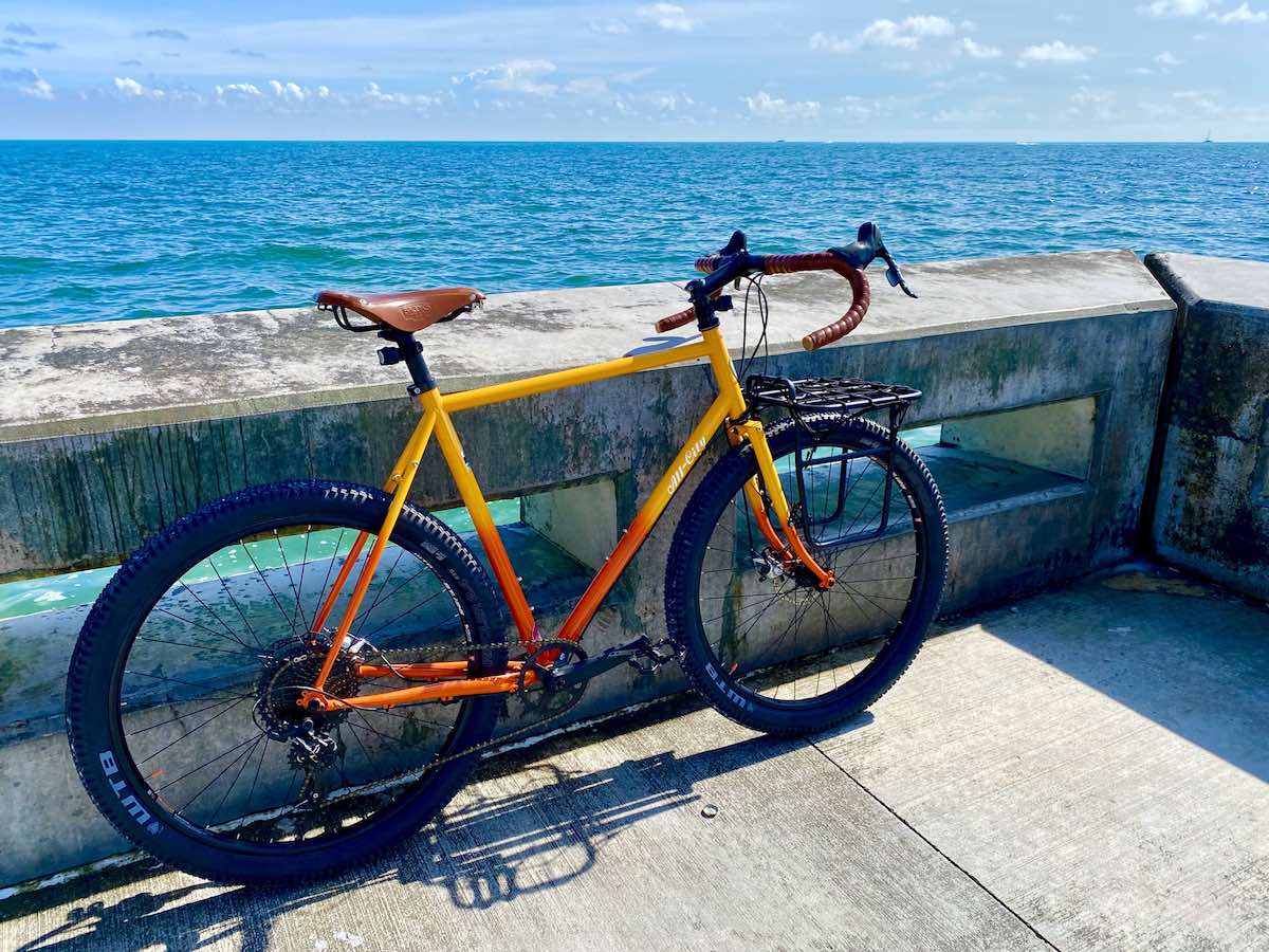bikerumor pic of the day an orange and yellow all city bicycle leans against the concrete wall overlooking bright clear blue ocean on a bright sunny day in key west florida.