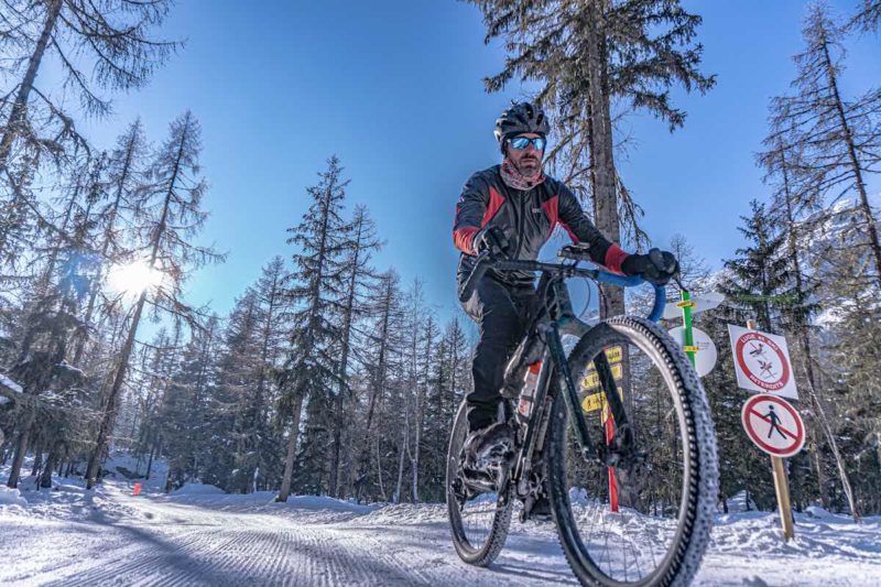 bikerumor pic of the day a mountain biker rides on compacted snow trail among pine trees on a clear sunny day in the chamonix valley france.