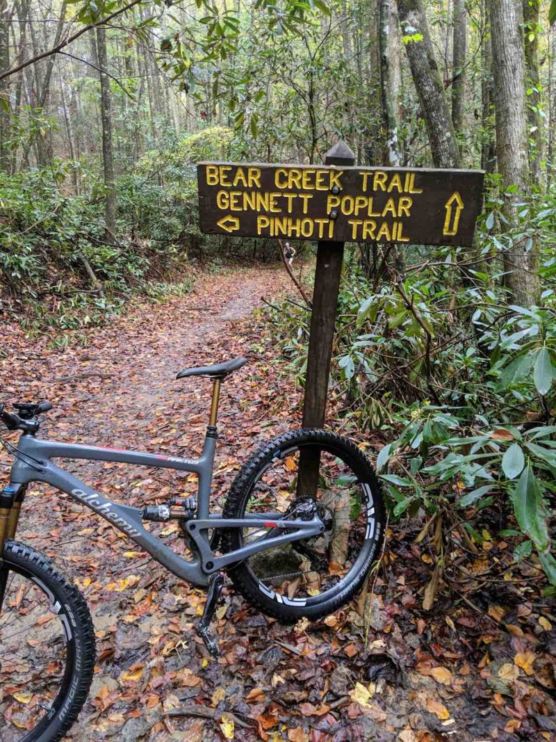 bikerumor pic of the day an alchemy mountain bike is leaning against a trail sign on the Pinhoti Trail system in North Georgia, on a leaf covered trail in the forest.