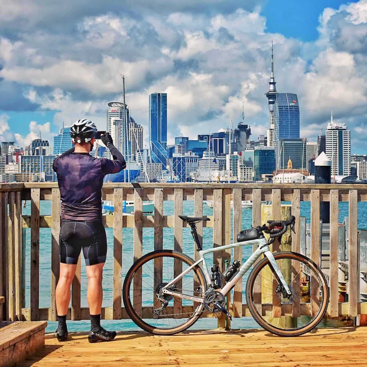 bikerumor pic of the day man and bicycle stand on a wooden pier overlooking the city of auckland new zealand on a bright sunny day