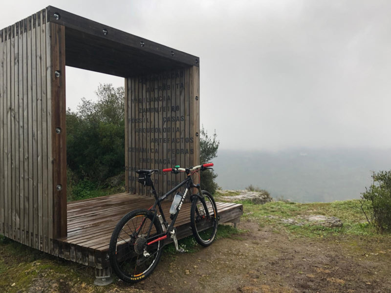 bikerumor pic of the day a bicycle leans against a square wooden structure at the top of a mountain looking over into the clouds in Arrábida park natural, Portugal