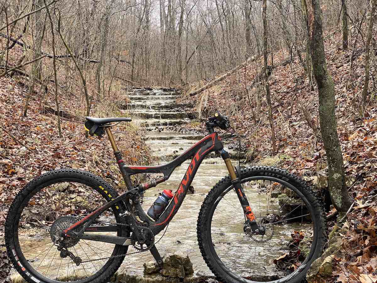 bikerumor pic of the day back 40 trail in oz, northwest arkansas a mountain bike is placed in front of a stepped stone waterfall stream in the woods with bare trees and dead leaves on the ground