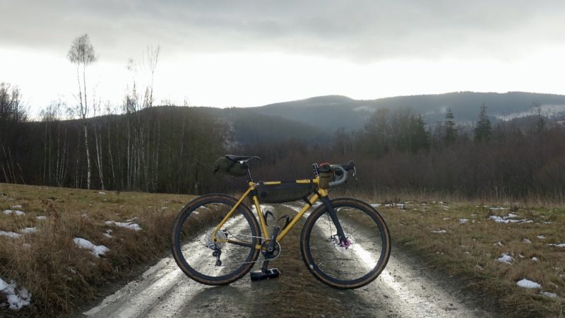 Rudawy Janowickie, Poland bikerumor pic of the day a yellow bicycle is posed across a wet dirt road with low mountains in the background