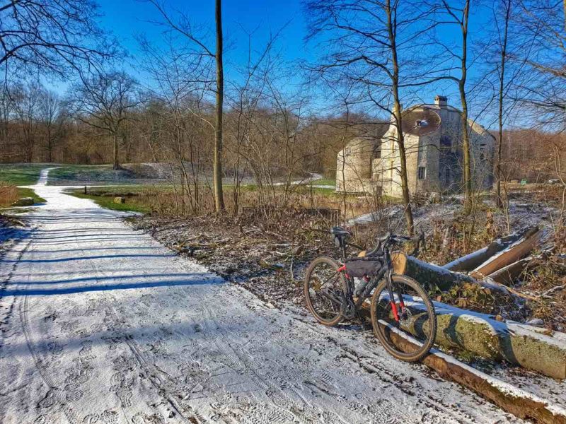 bikerumor pic of the day a bicycle leans against a log along a snow packed path near a chateau Photo taken at Château de la Chasse / Forêt de Montmorency / France.