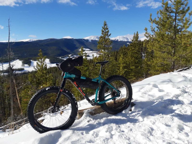 bikerumor pic of the day West Bragg Creek, Alberta, Canada, a salsa fat bike is on a snow packed trail with a view of the mountain beyond and pine trees on the horizon, the sky is clear and blue and it is sunny.