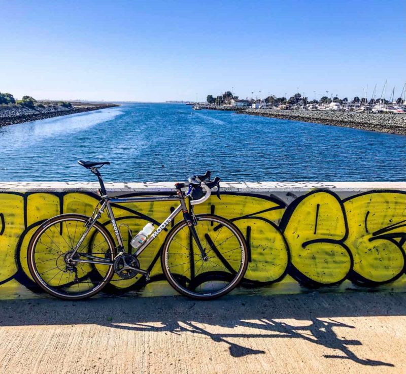 bikerumor pic of the day a bicycle leans against a concrete barrier with yellow graffiti on it overlooking a body of water.