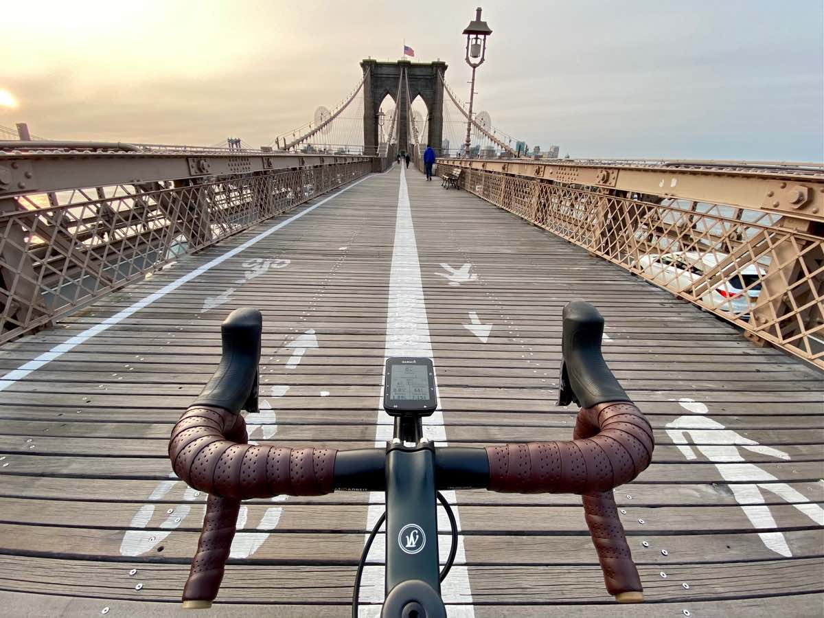 bikerumor pic of the day a photo of the handlebars of a bicycle positioned in the center of the brooklyn bridge in new york city at dusk.