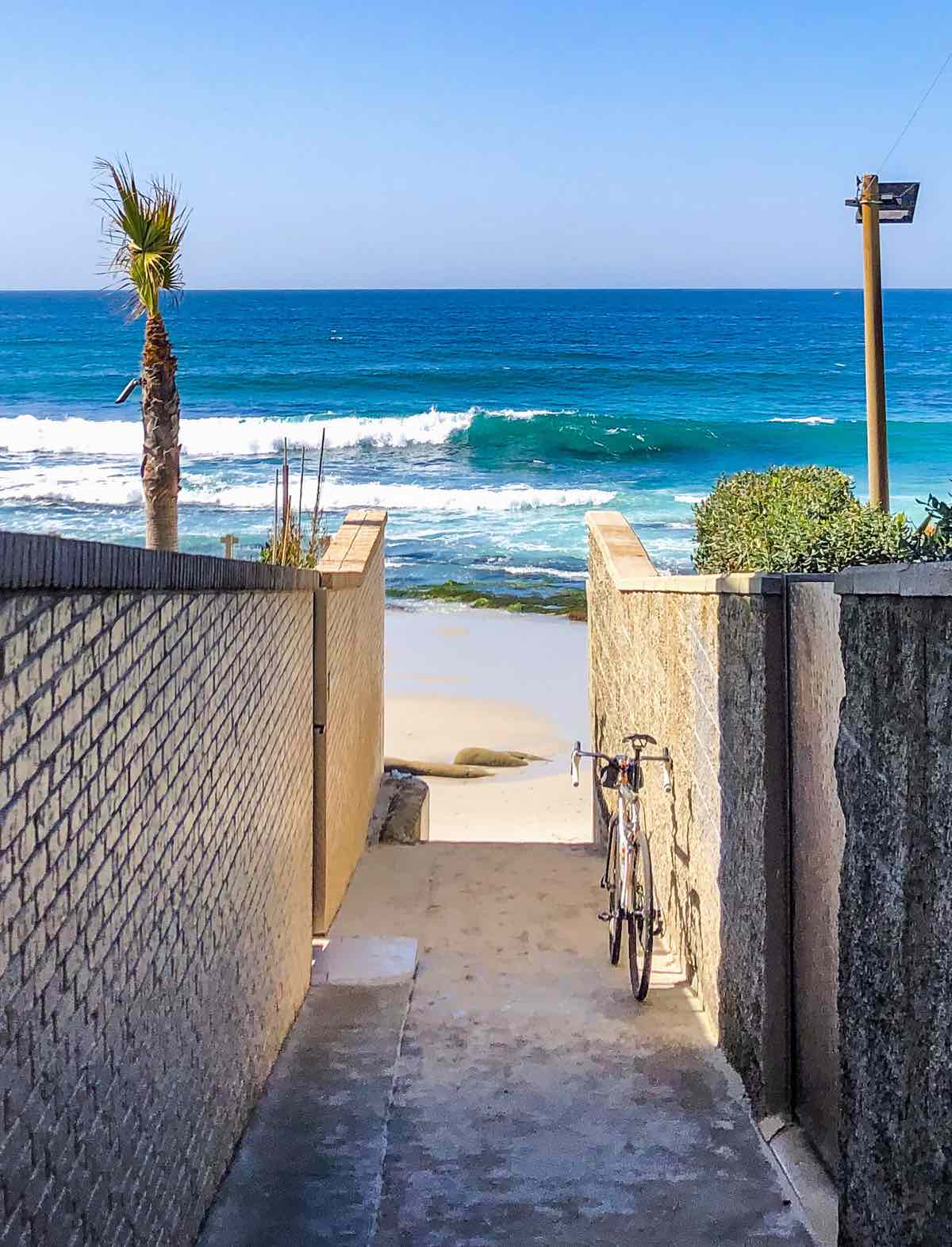 bikerumor pic of the day a bicycle leans against a brick wall hallway that leads to the ocean in Late Feb in La Jolla California the ocean is bright blue with a cloudless sky.