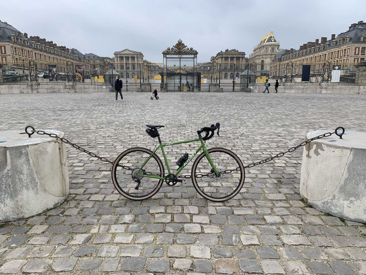 bikerumor pic of the day a ratchet outback bicycle leans against a chain fence on a cobblestone square leading to the Palace of Versailles in paris france. the gates are closed and there are only a handful of people walking around the square on an overcast day
