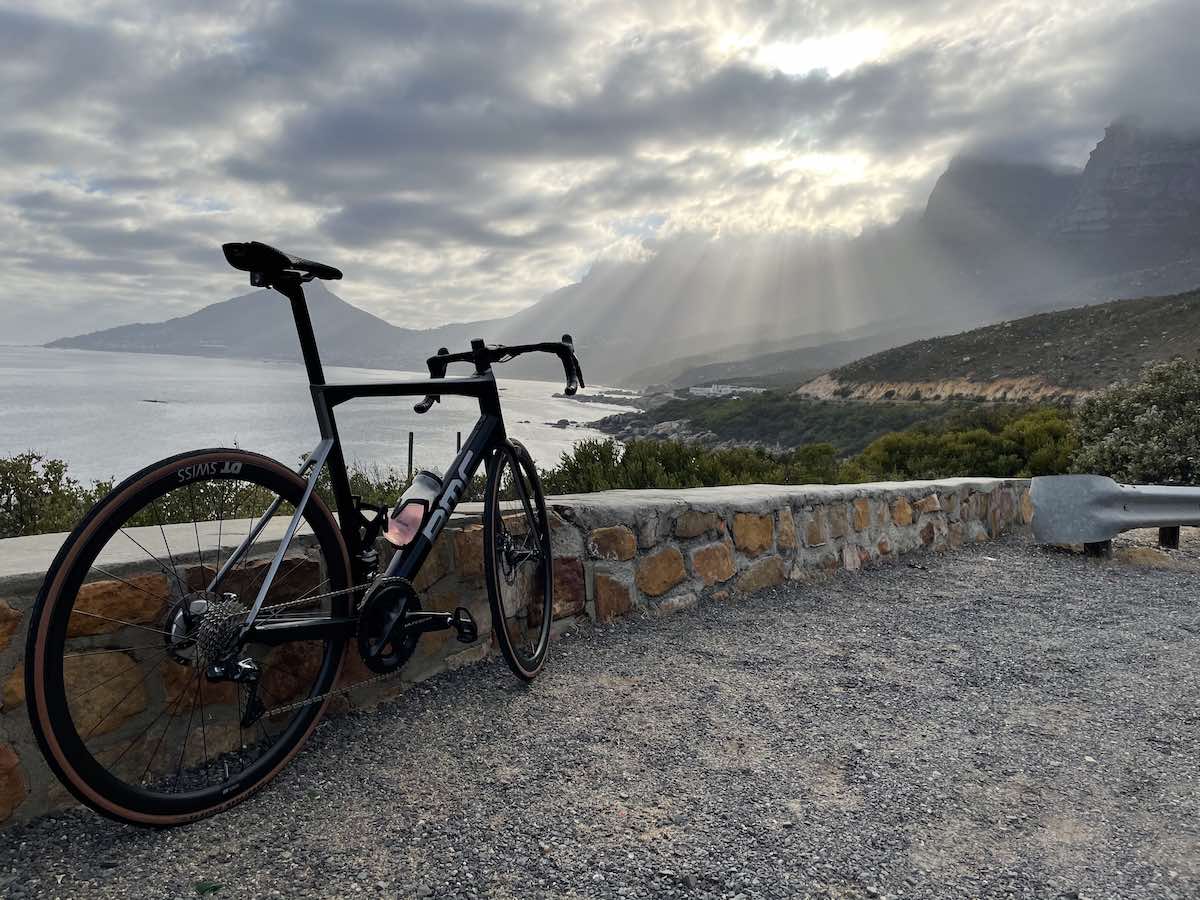 bikerumor pic of the day a bcc road bike leans against a low rock wall overlooking a bay surrounded by mountains the sky is cloudy and the sun is shining through with rays spreading out in the distance