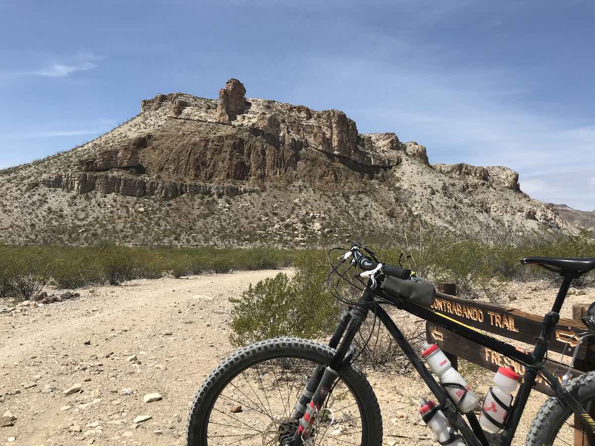 mountain bike next to a trail sign in beg bend ranch state park texas by a dirt trail with a rocky mountain in the distance